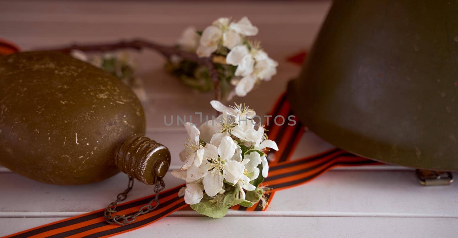 Composition to victory day. Soldier's flask, helmet and branches of apple trees and on a white background. banner size. High quality photo