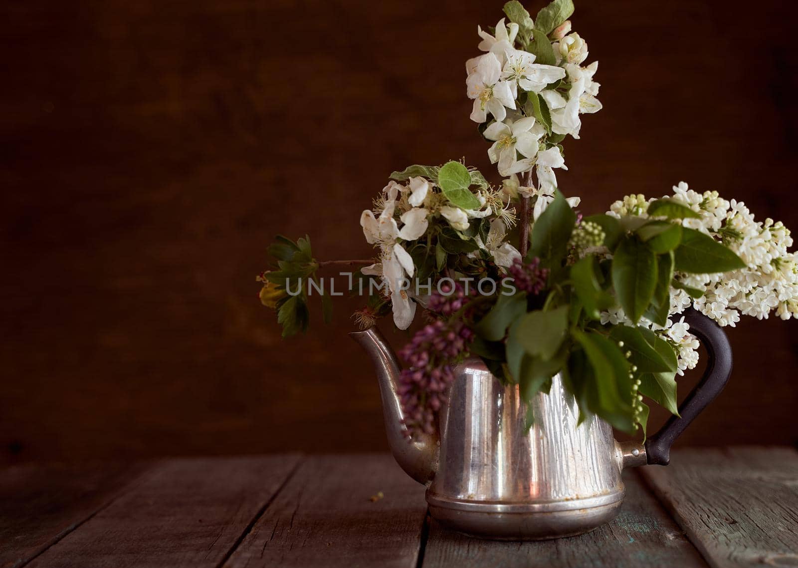 apple blossoms, cherries and lilacs in an iron teapot on a brown background. High quality photo