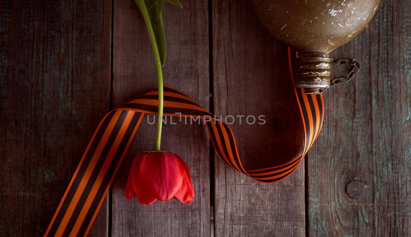 Red tulip and soldier's flask with black orange ribbon. On a wooden table by Xelar