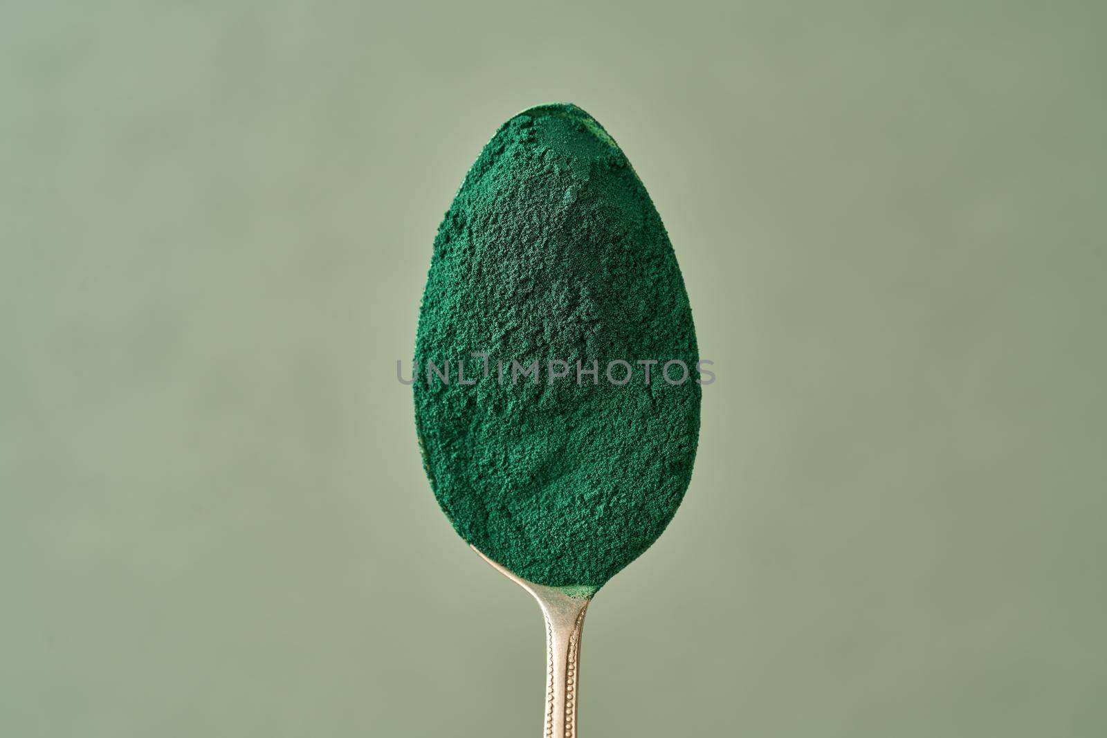 Spirulina powder on a spoon above a green background, with copy space by madeleine_steinbach