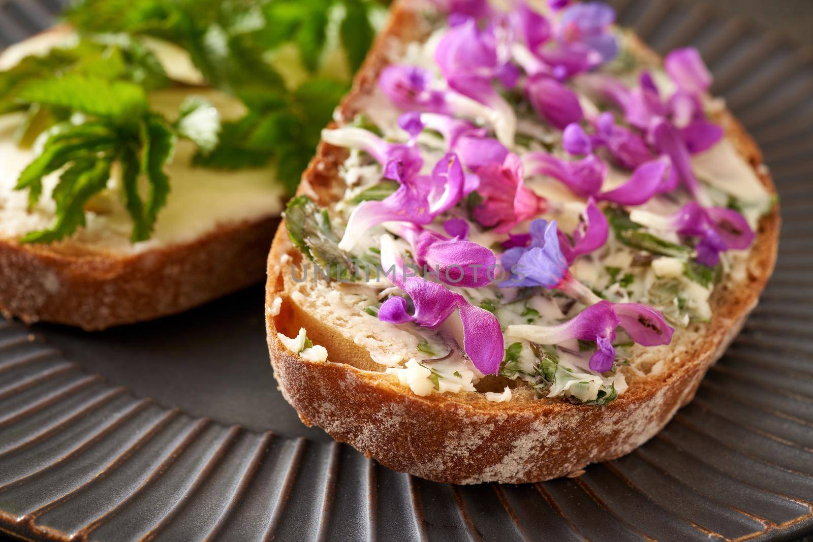 A slice of sourdough bread with butter and purple dead-nettle and lungwort flowers, with ground elder leaves in the background