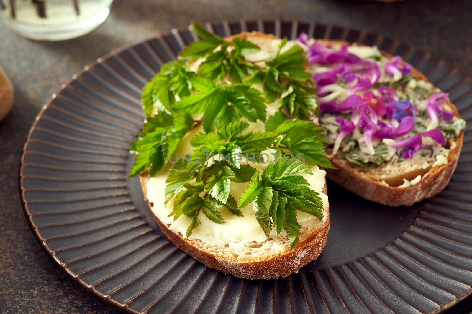 Slice of sourdough bread with young goutweed leaves - a wild edible spring plant, with purple dead-nettle in the background by madeleine_steinbach