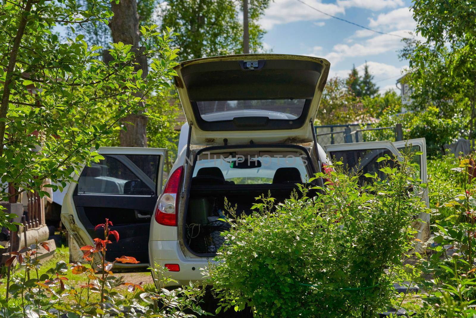 White car with open doors, trunk and hood stands on a garden plot by vizland