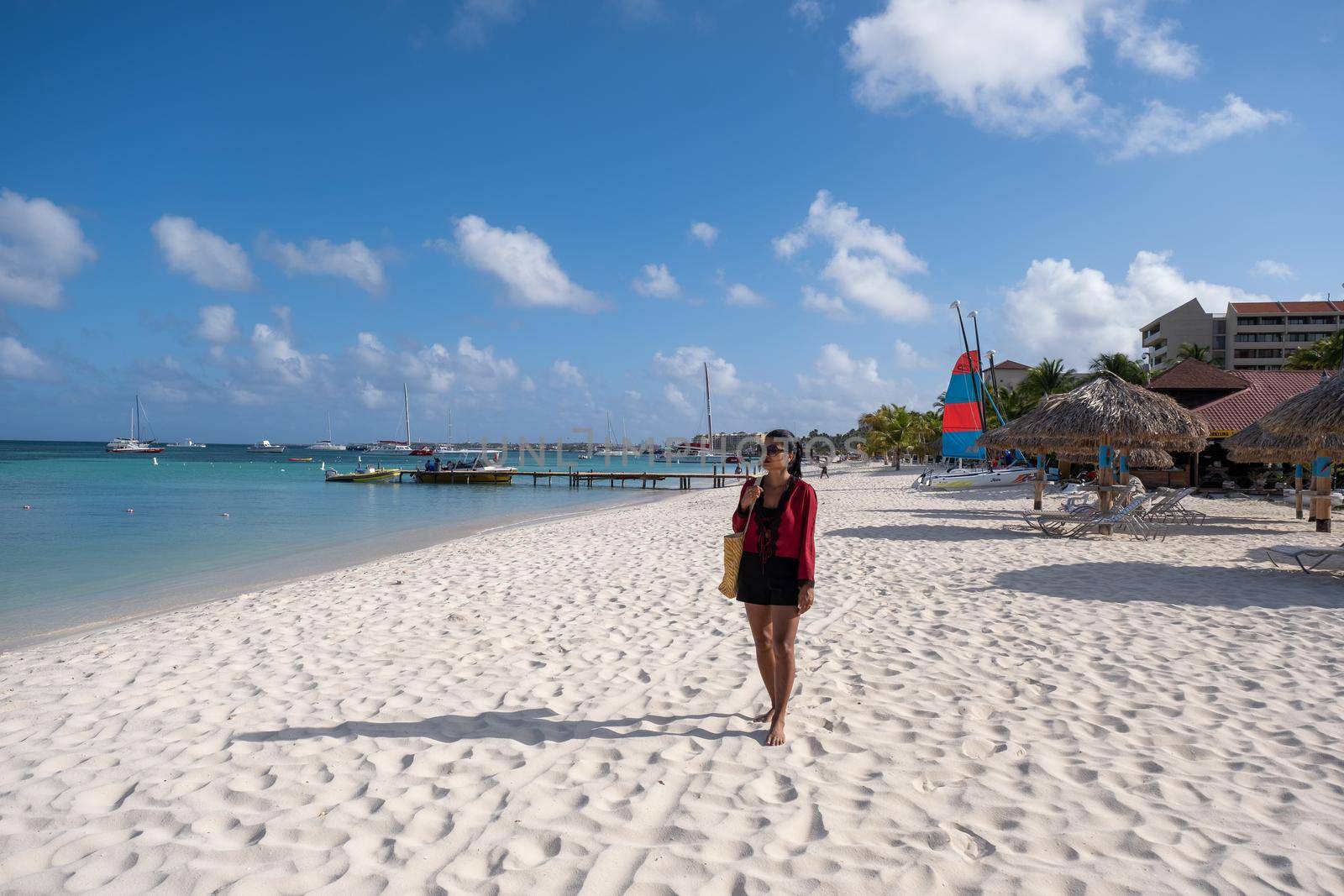 Palm Beach Aruba, Amazing tropical beach with palm trees entering the ocean against azur ocean, gold sand, and blue sky.
