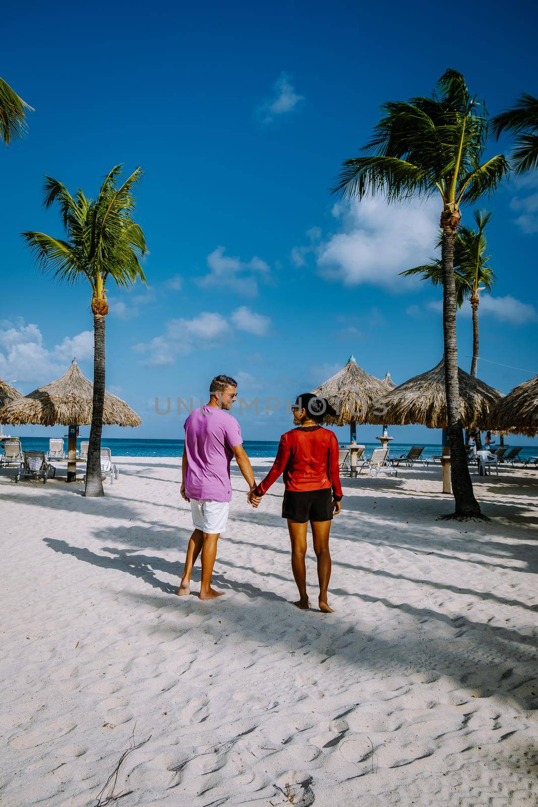 Palm Beach Aruba, Amazing tropical beach with palm trees entering the ocean against azur ocean, gold sand, and blue sky. man and woman walking at a white beach, mid age couple