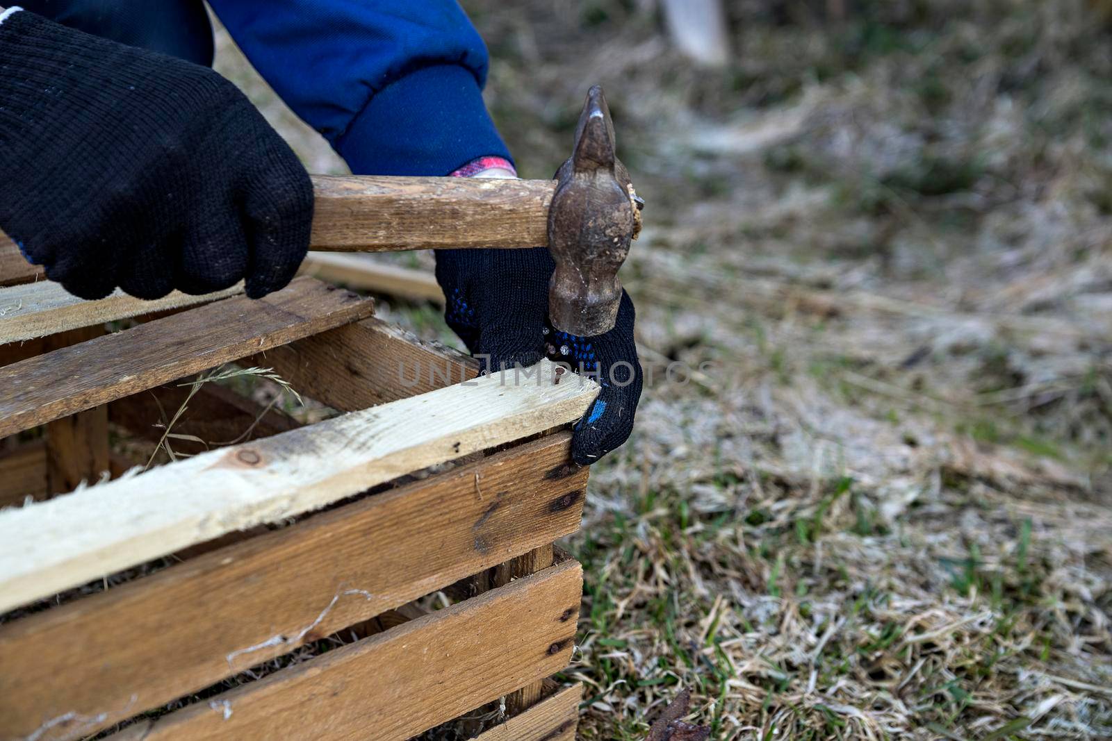Man hammers nail into bar of wooden box. Hands in black gloves.
