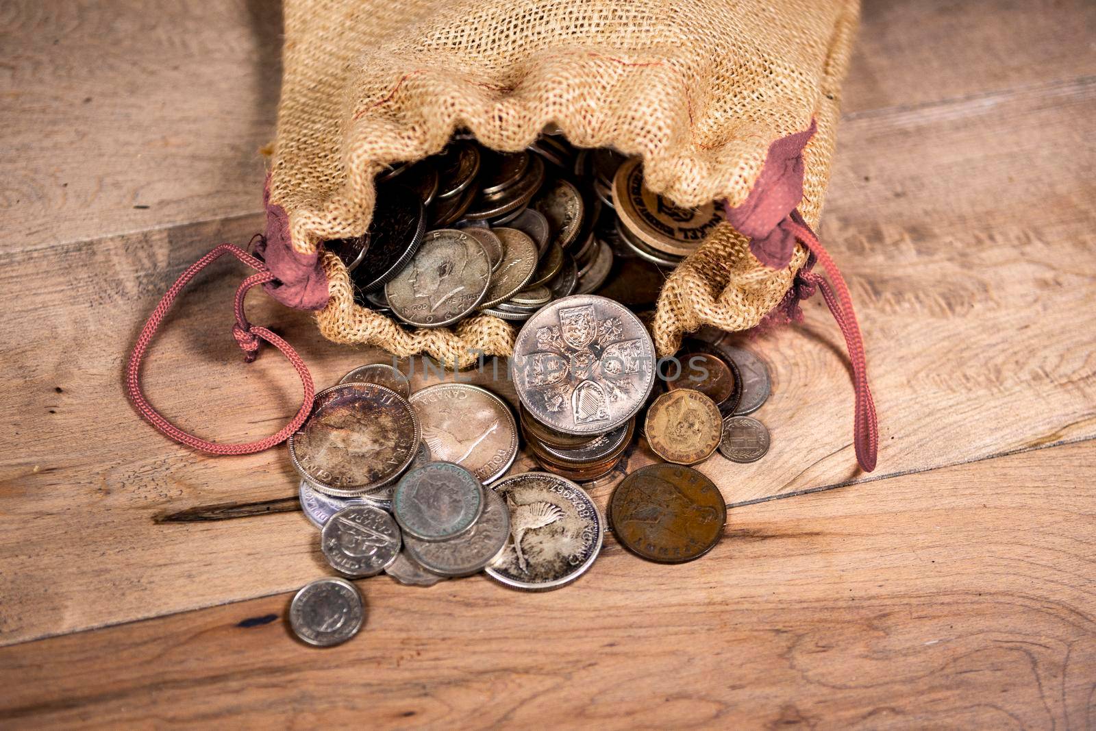 A collection of old  and new coins lies in a canvas bag on the floor