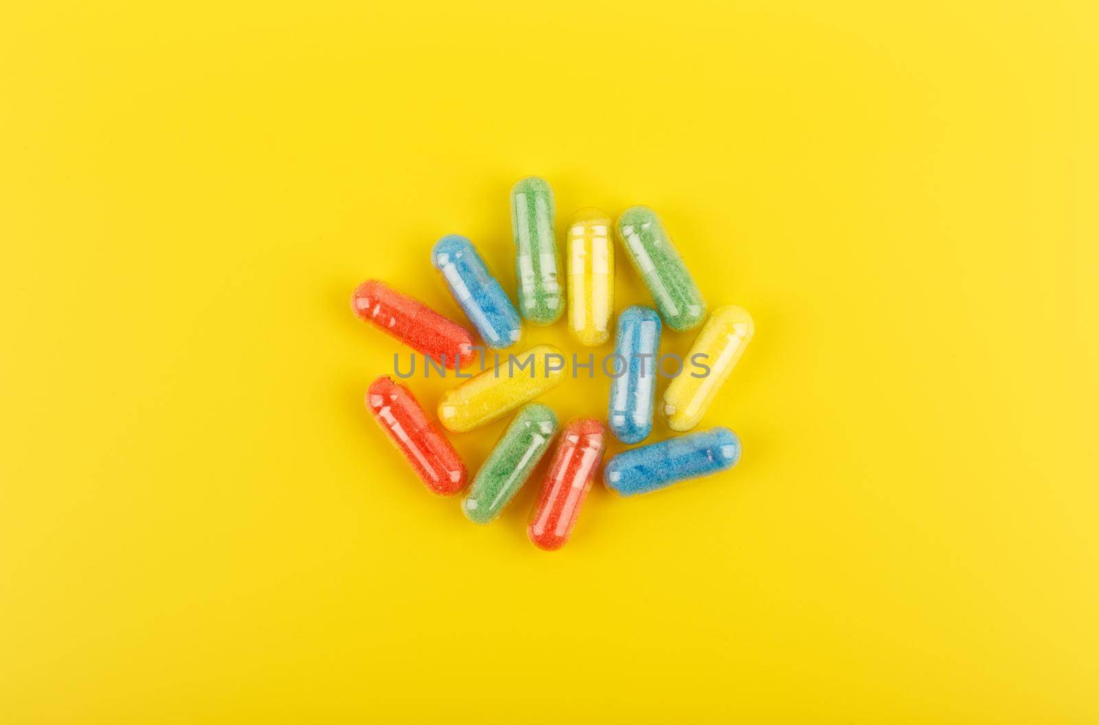 Flat lay with multicolored oval pills against yellow background. Concept of vitamins and wellbeing. Spilled pills flat lay on yellow background