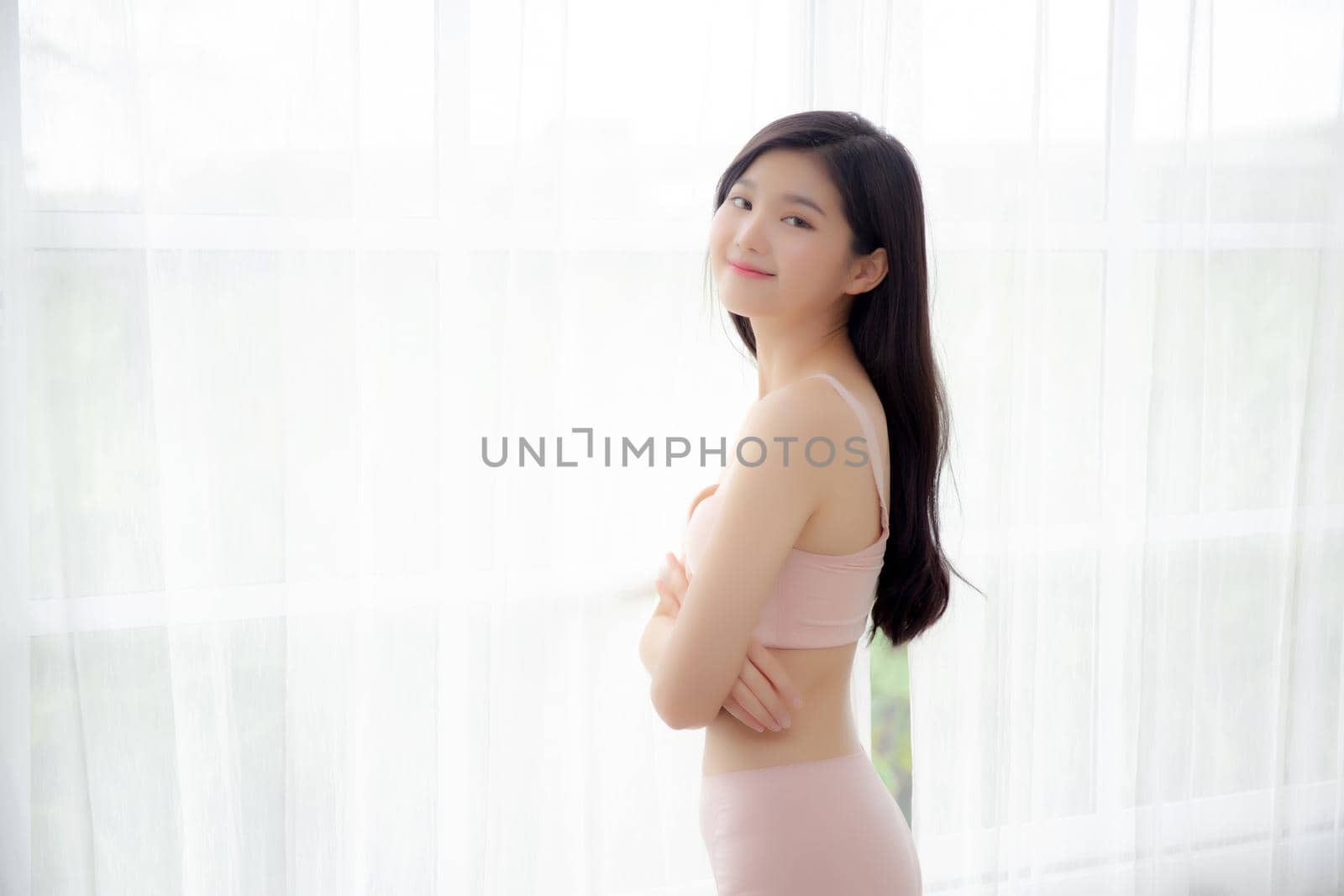 Beautiful portrait young asian woman sexy standing the window and smile while wake up with health, body of girl happy with freshness and cheerful with wellbeing, lifestyle and relax concept.