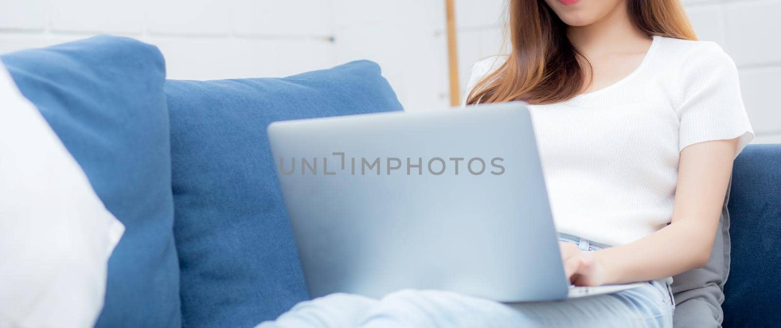 Young asian business woman smile and work from home with laptop computer online to internet on sofa in living room, freelance girl using notebook on couch with comfort, new normal, lifestyle concept.