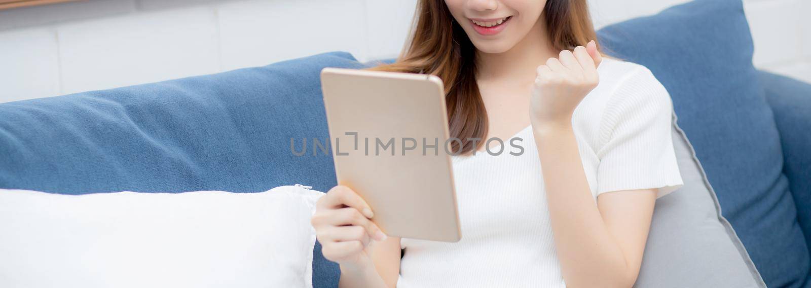 Young attractive asian woman resting using browsing tablet computer on sofa at home, happy girl sitting on couch relax reading digital gadget with excited at house, communication and lifestyle concept. by nnudoo