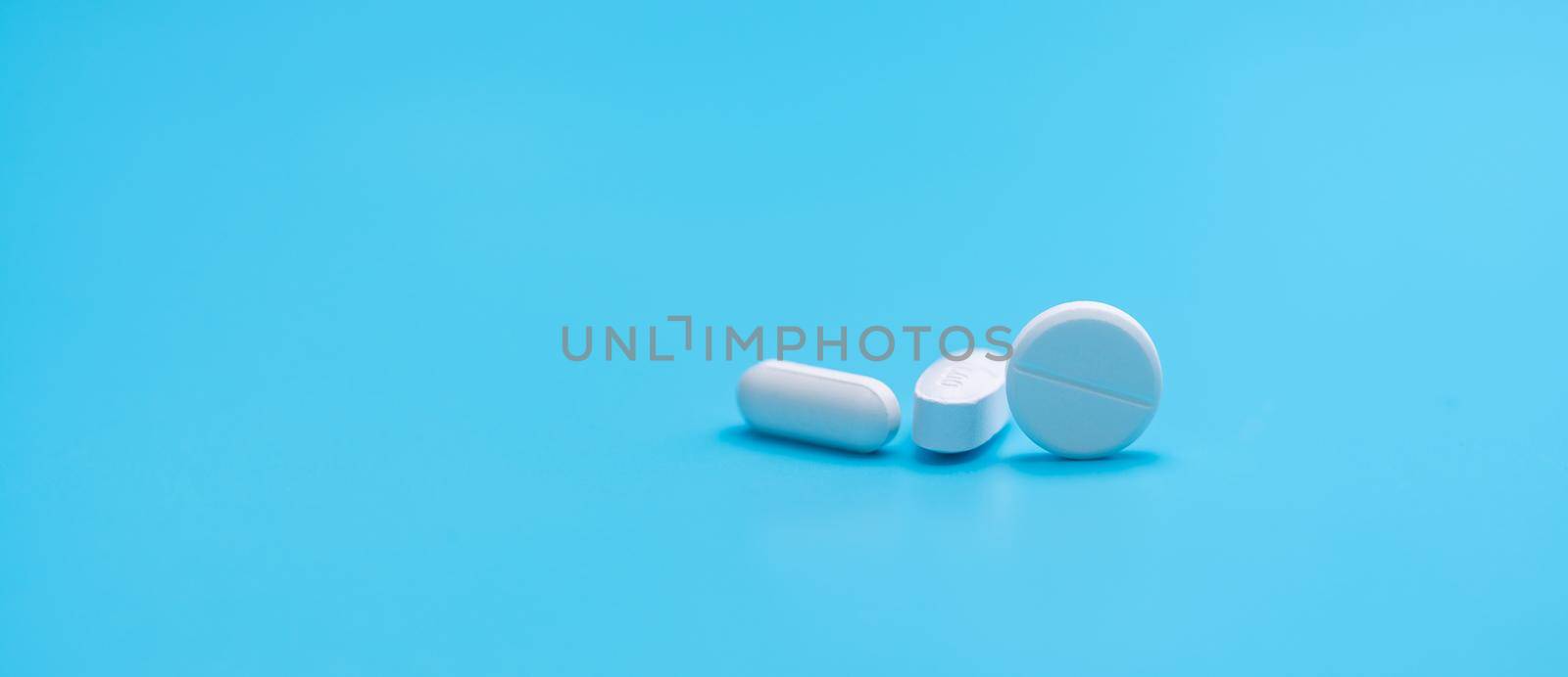 Round white tablets pills and oval tablets pills on blue background. Pharmacy shop banner. Prescription drugs. Pharmaceutical industry. Painkiller, antibiotics, and antacid tablet pills. Pharmaceutic. by Fahroni