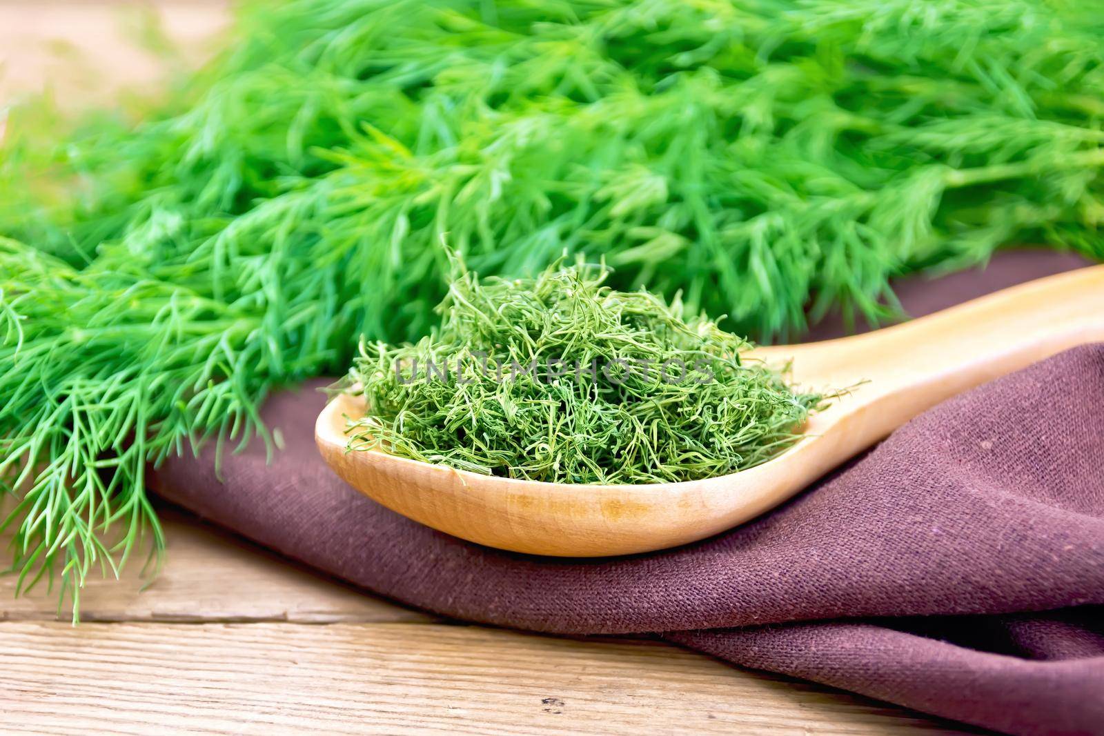 Dry dill in a spoon on a napkin, fresh herb on a wooden board background