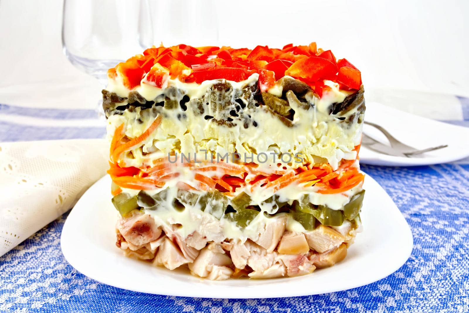 Layered salad with chicken, egg, mushrooms and cucumber, carrots and pepper, mayonnaise on the background of the tablecloth