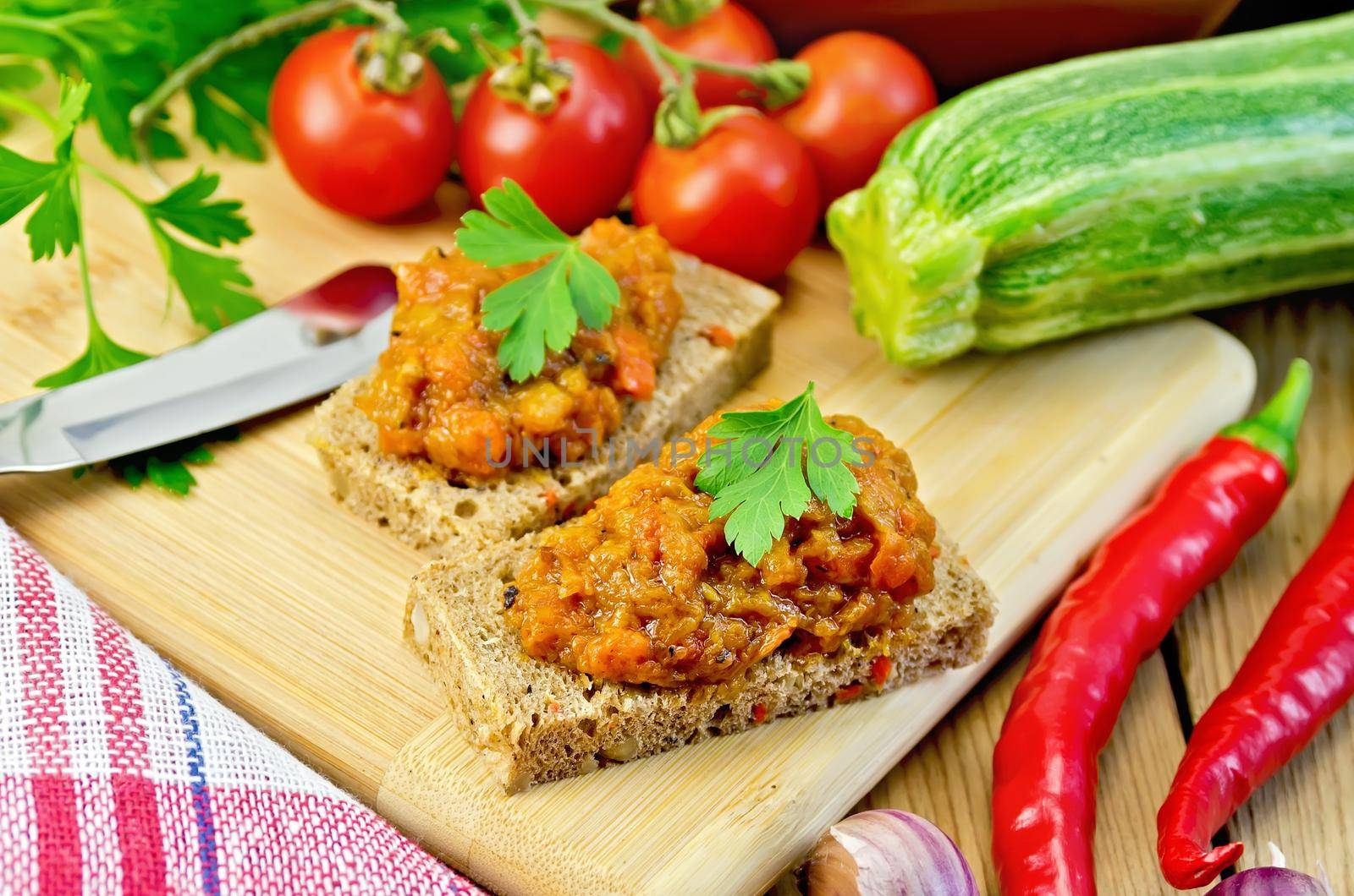 Sandwich with caviar and parsley squash, garlic, tomatoes, pepper, knife, zucchini on a wooden boards background