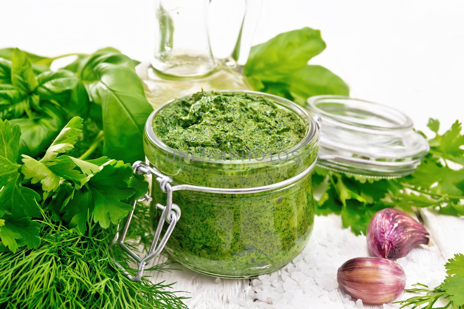 Sauce of dill, parsley, basil, cilantro, other spicy herbs, garlic and vegetable oil in a glass jar, coarse salt on wooden board background