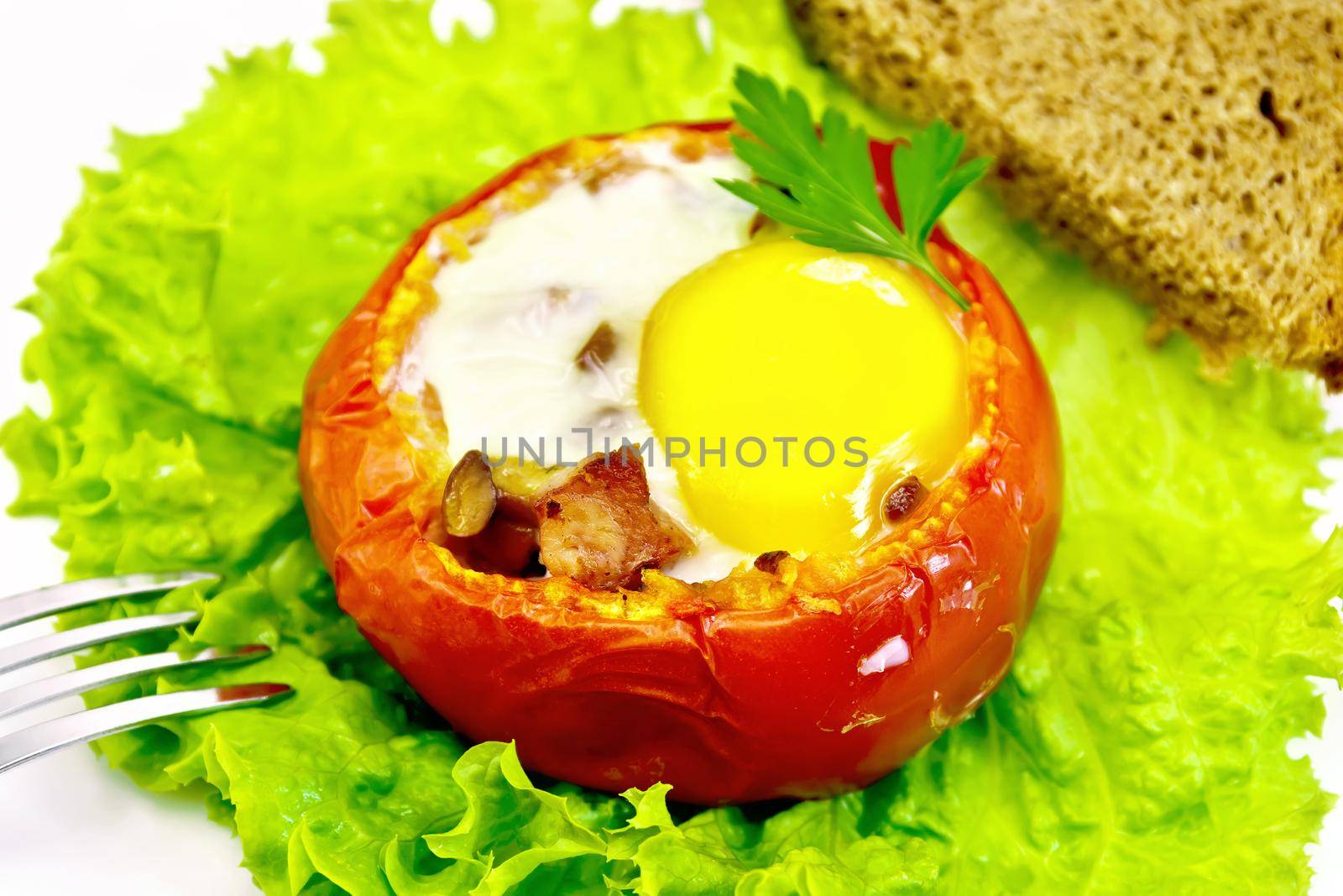 Scrambled eggs with ham and mushrooms in a tomato on a green lettuce in the plate, fork and bread