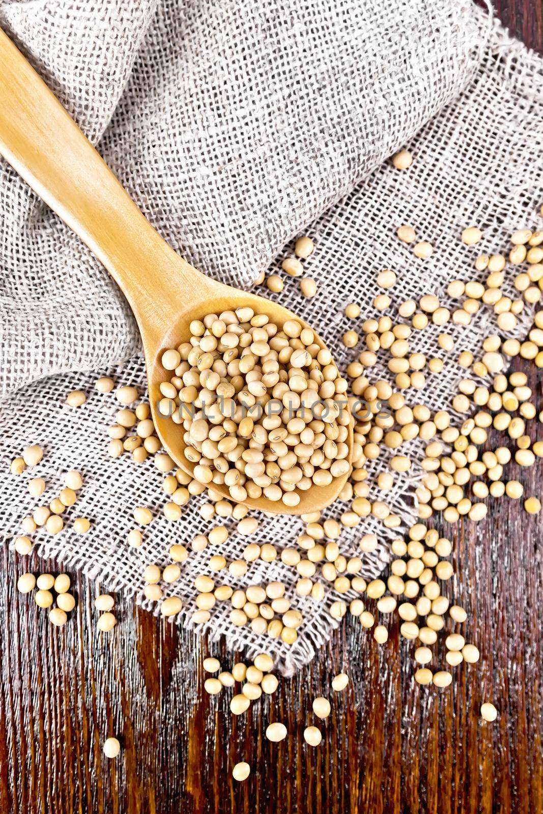 Soy beans in a spoon on sacking on a wooden board background from above