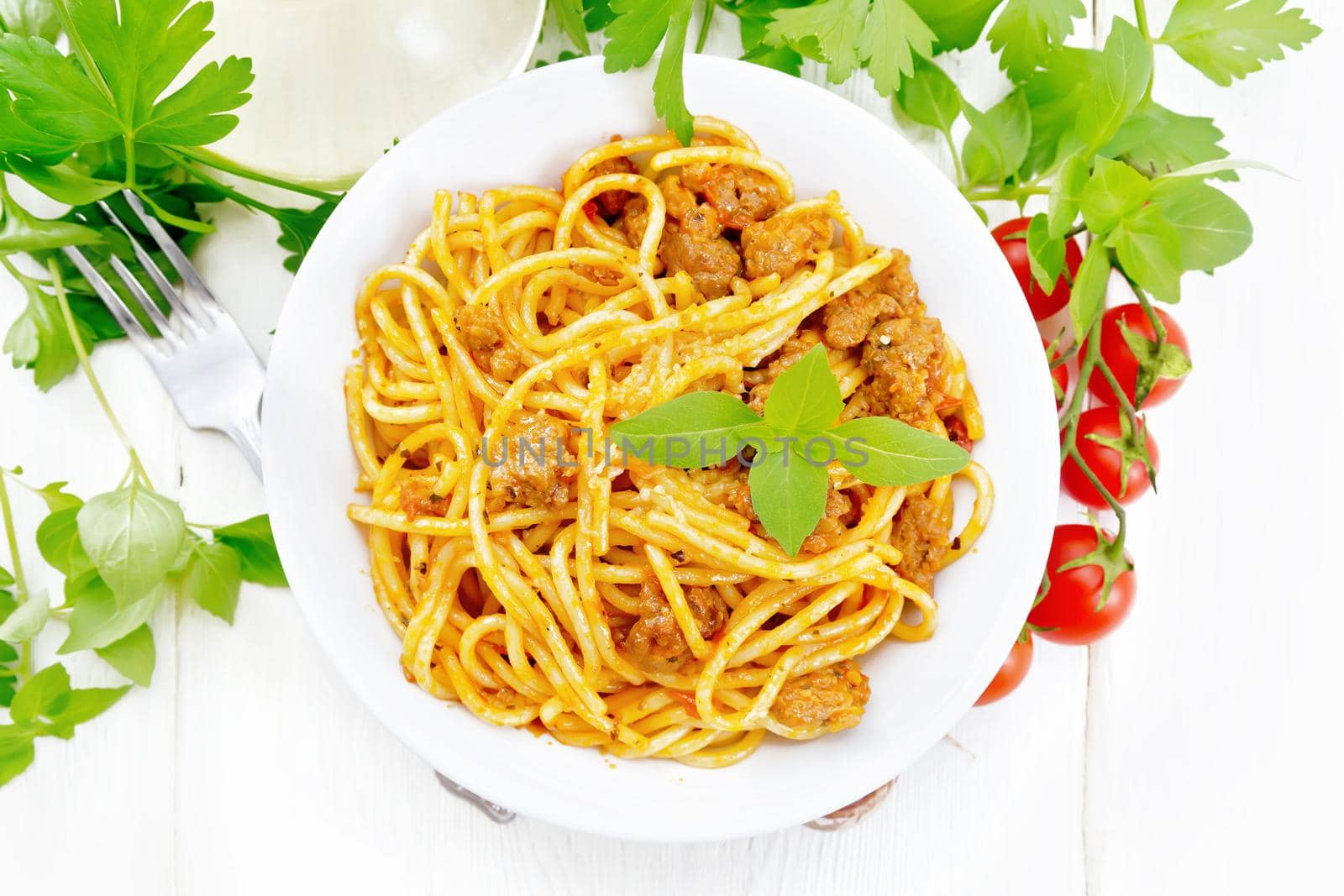 Spaghetti pasta with sauce Bolognese of minced meat, tomato juice, garlic, wine and basil in a plate, vegetable oil, spicy herb on a wooden board background from above