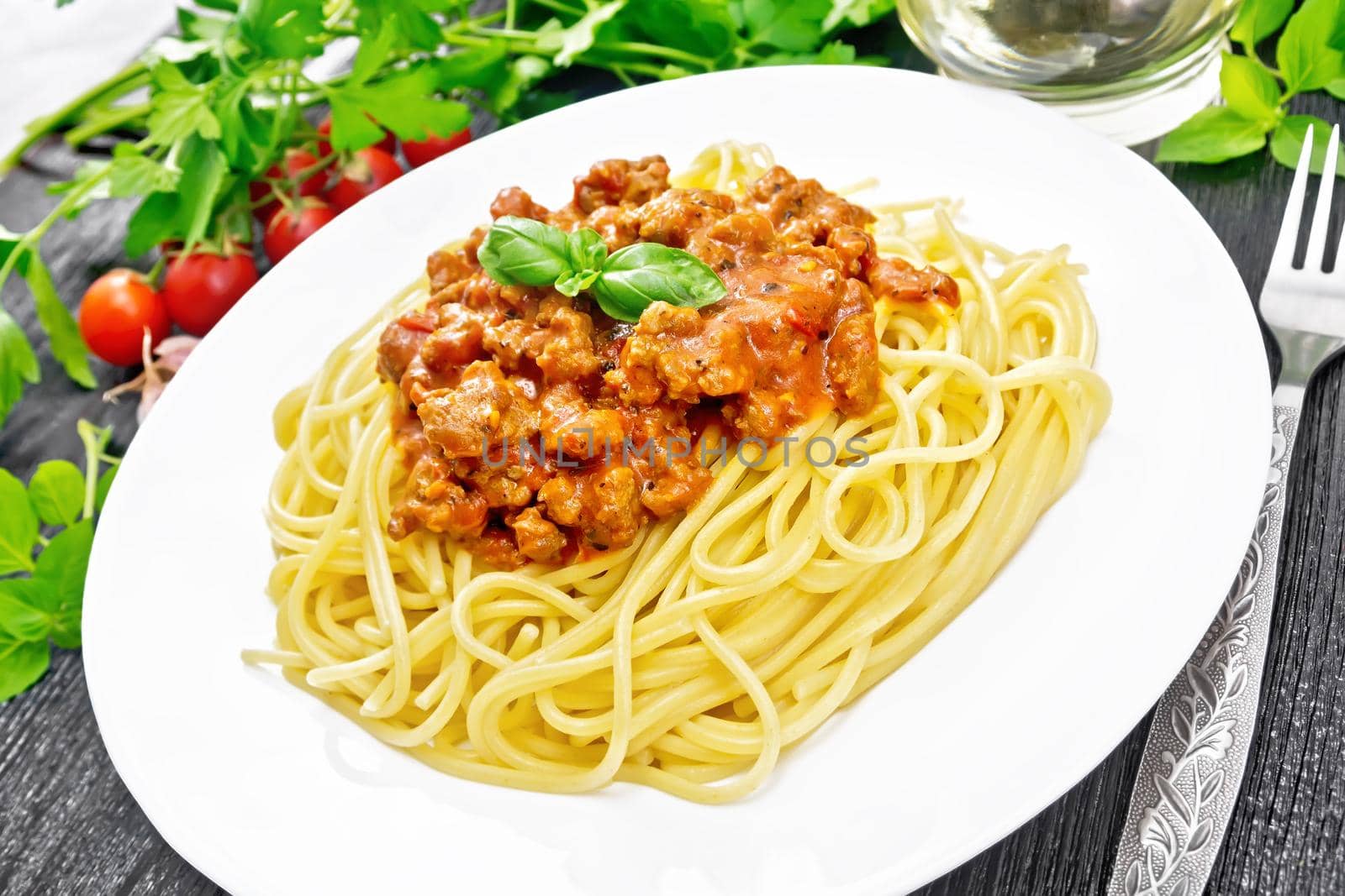 Spaghetti pasta with Bolognese sauce of minced meat, tomato juice, garlic, wine and spices in a plate, vegetable oil, spicy herb on a wooden board background