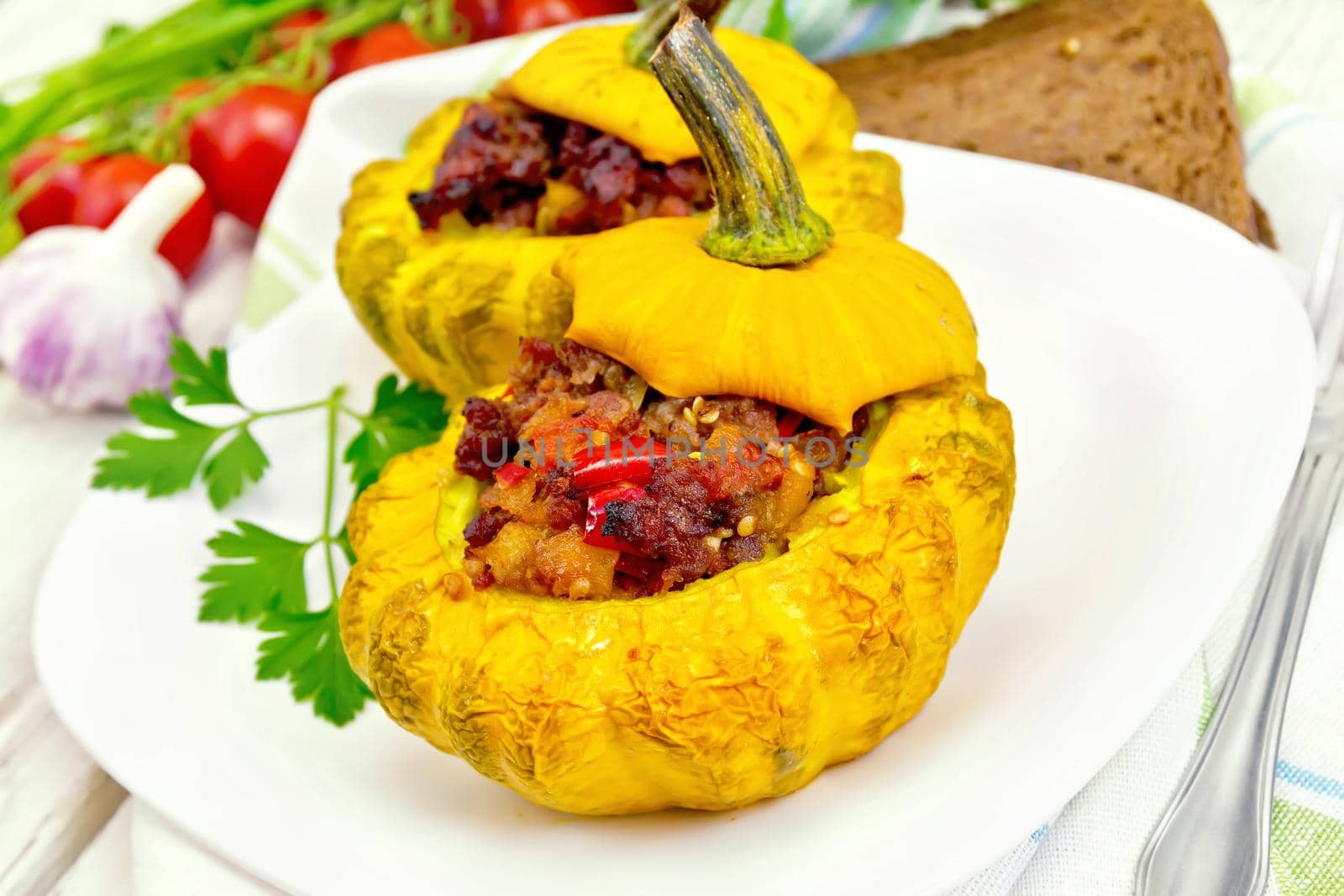 Two yellow squash stuffed with meat, tomatoes and peppers in the dish, bread, garlic, parsley and a napkin on a wooden boards background