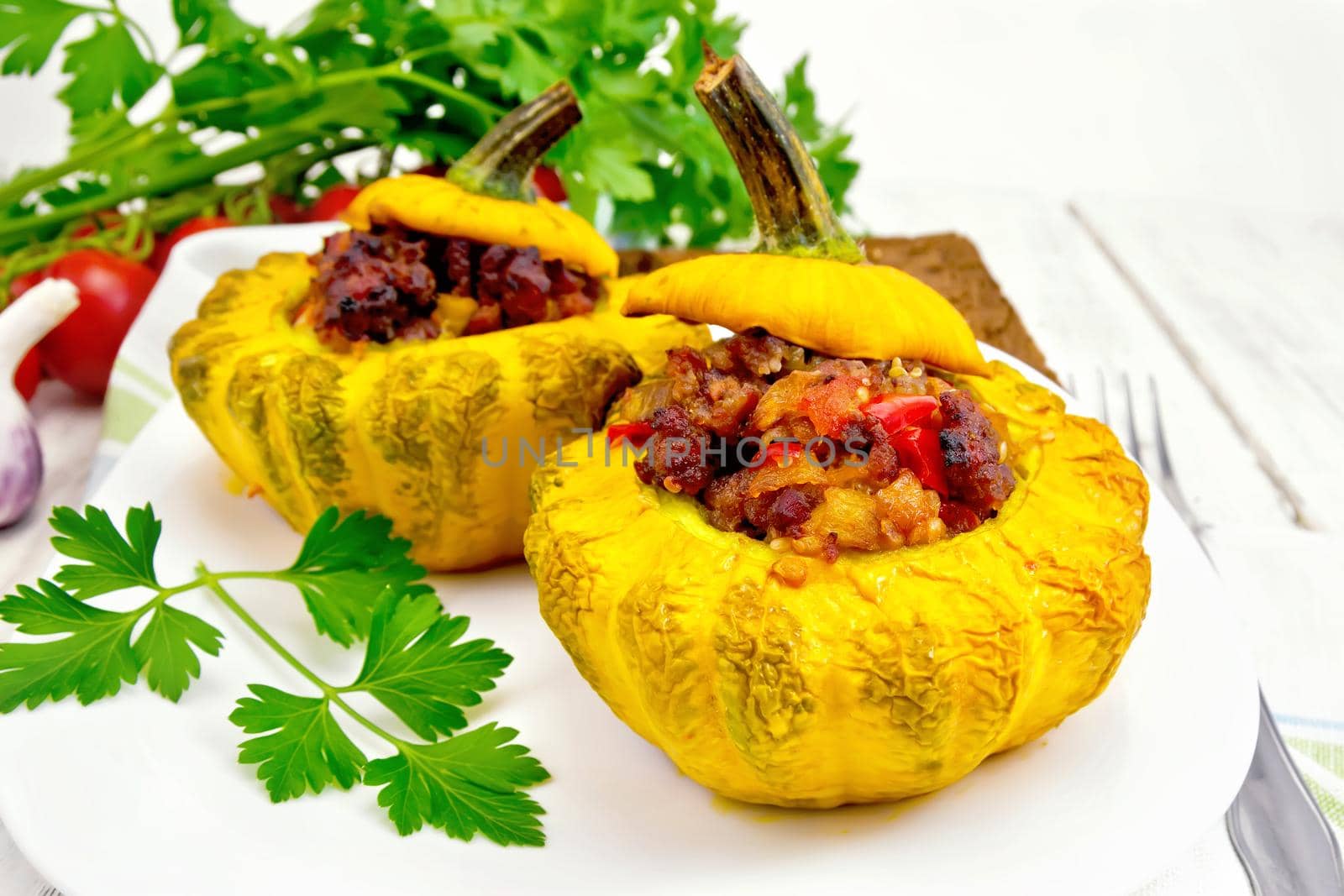 Two yellow squash stuffed with meat, tomatoes and peppers in the dish, bread, garlic, parsley and fork on the background of wooden boards