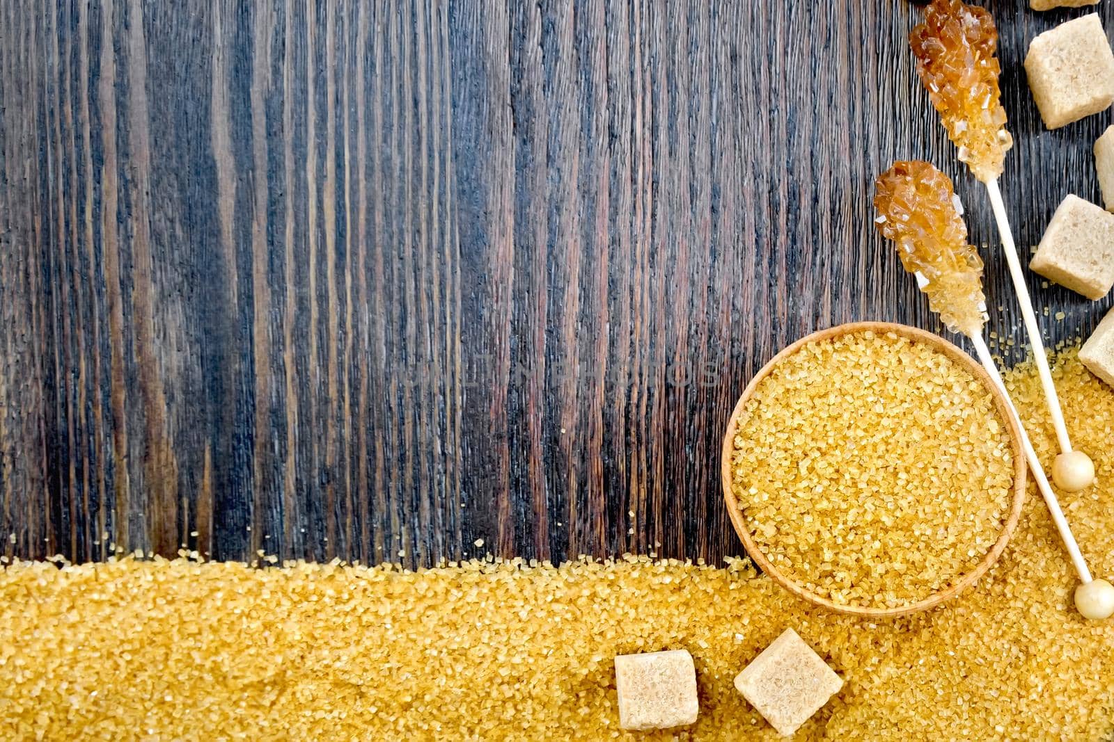 Sugar brown granules in a bowl, cubes and crystals on a stick in the form of a frame on the background of a wooden board