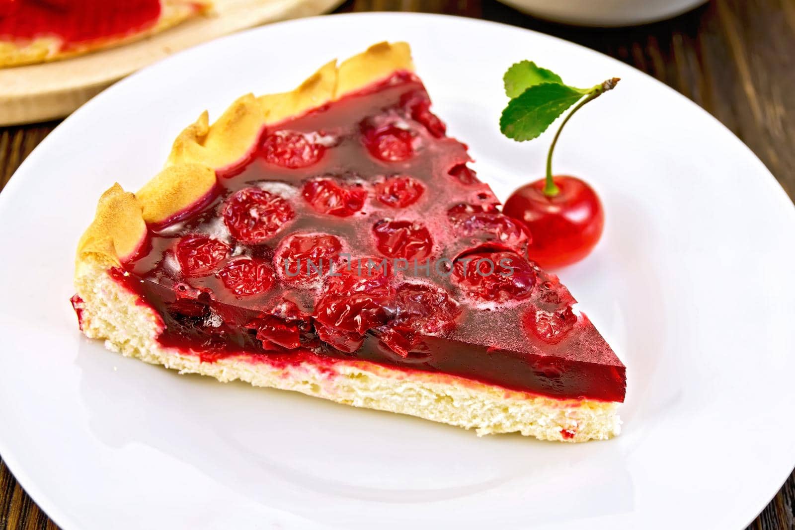 Piece of sweet pie with cherry berries and jelly in a plate with a fork on a dark wooden board