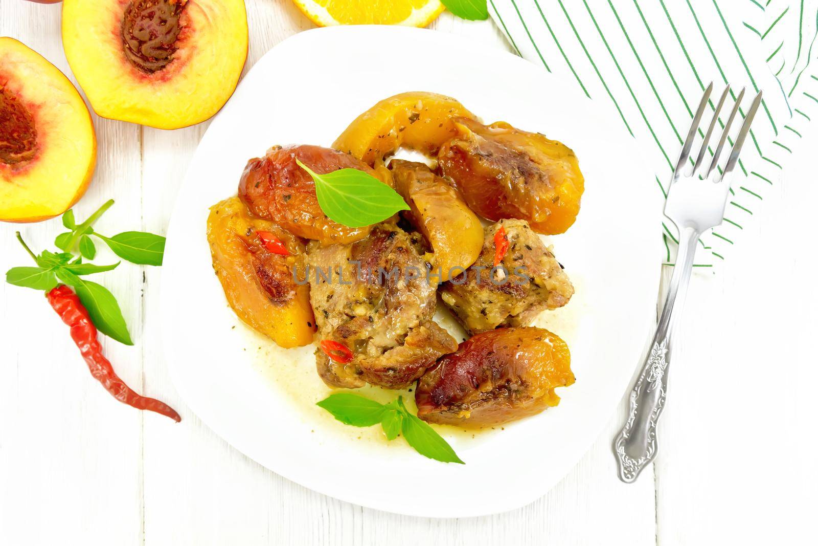 Turkey stewed with peaches, fresh hot pepper and orange sauce, basil leaves in a plate, napkin, fruits on wooden board background from above