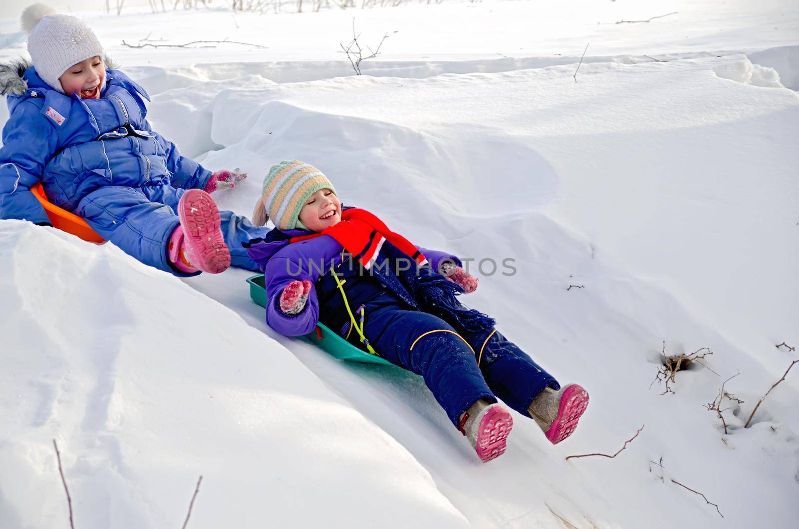 Two little girls on a sled sliding down a hill on snow in winter