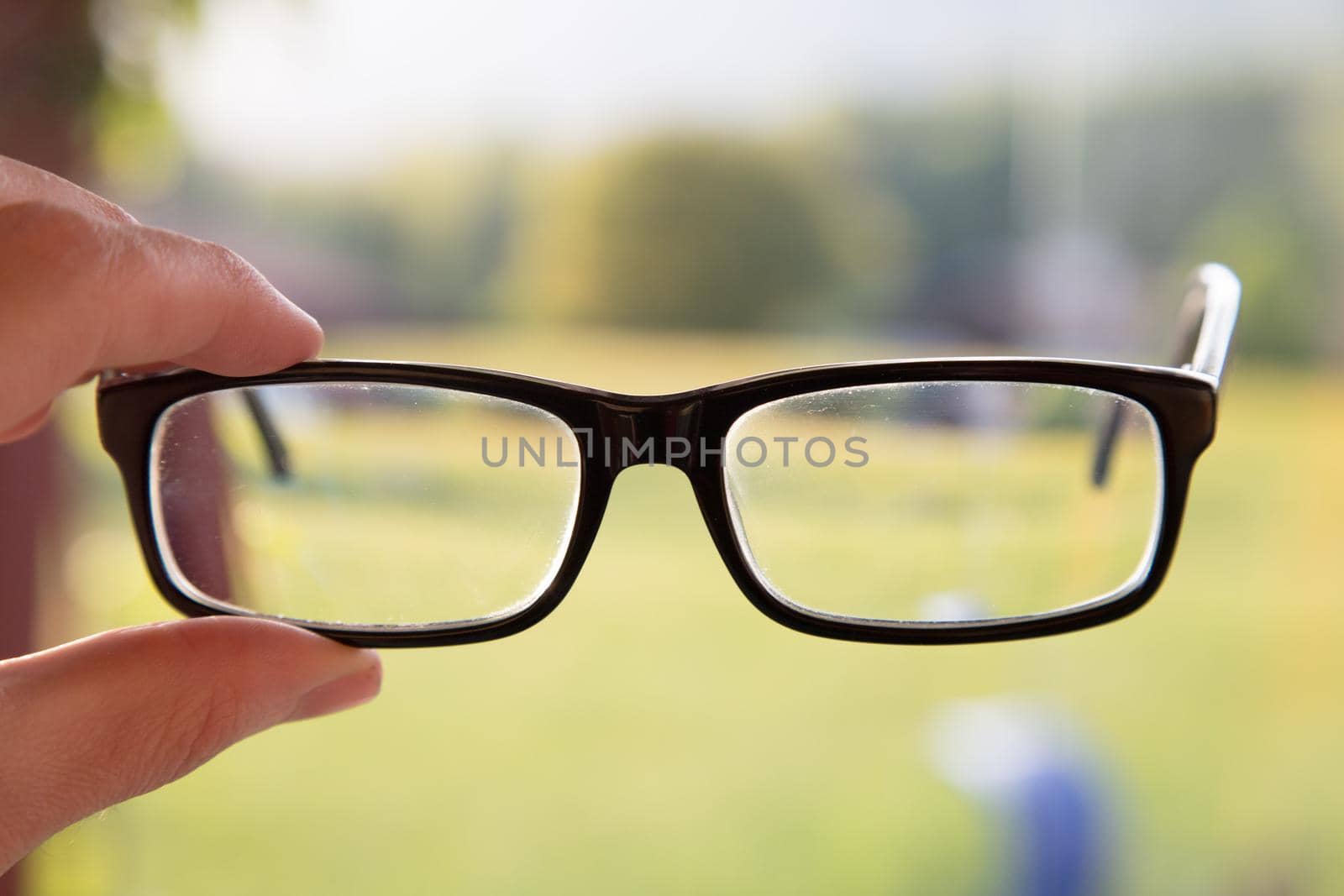 Young man holding his glasses outdoors, blurry background