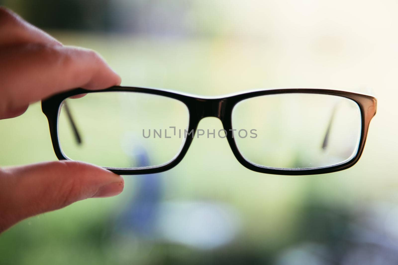 Young man holding his glasses outdoors, blurry background