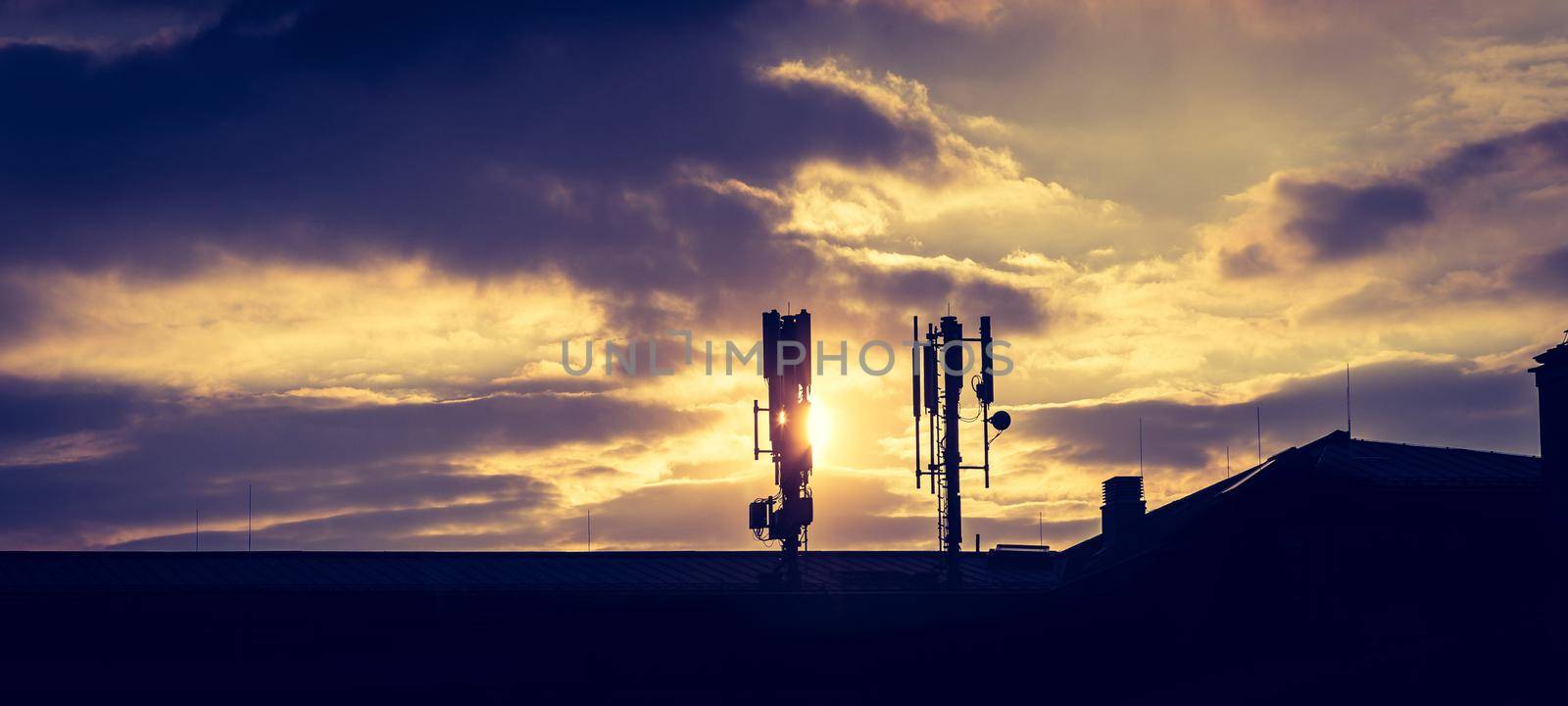 Silhouette of communication or cell tower on the rooftop of a building, evening sunshine