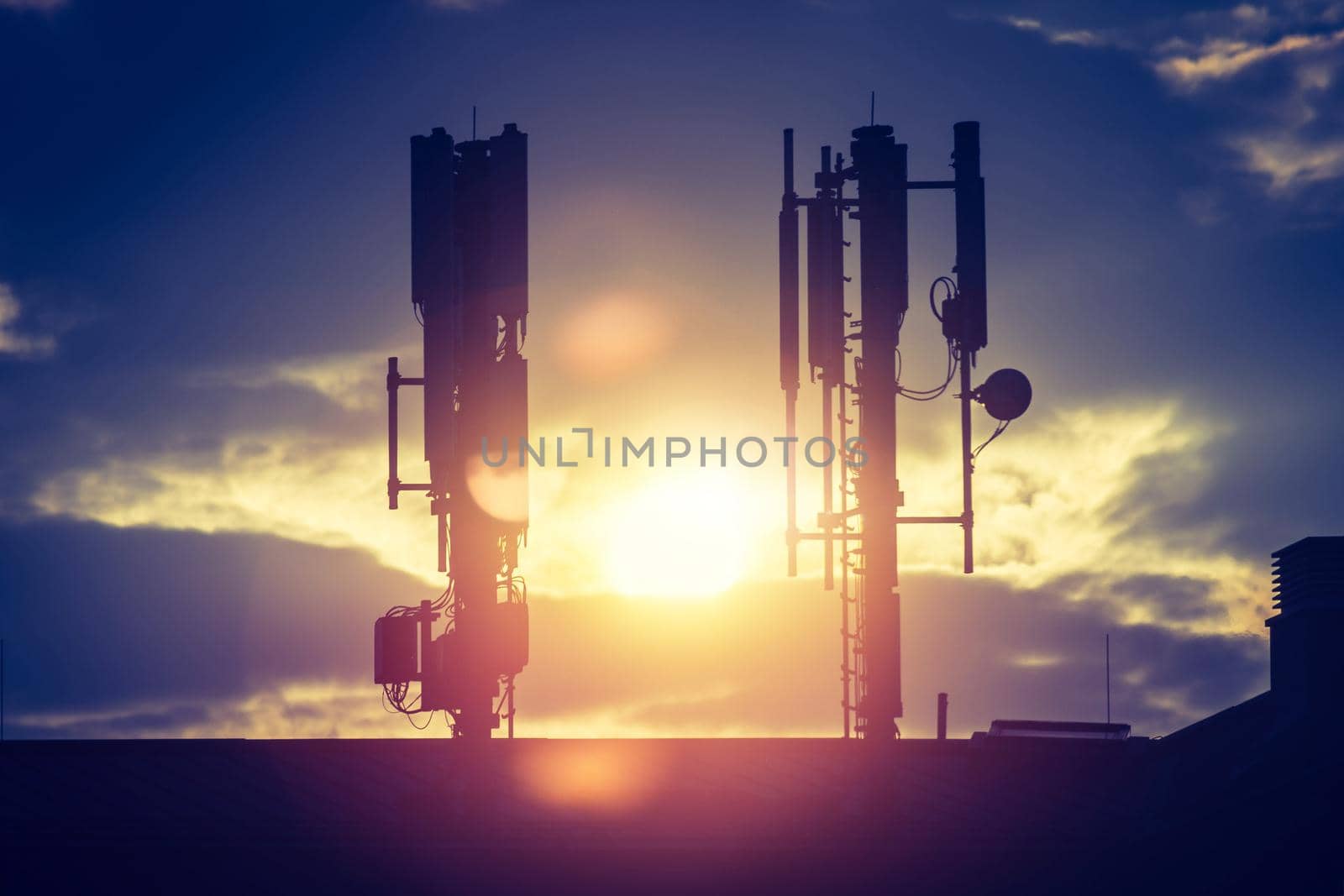 Silhouette of communication or cell tower on the rooftop of a building, evening sunshine