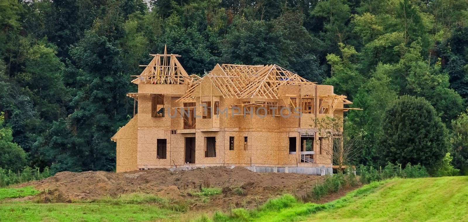 New residential house under construction. Wooden framework of the building on green lush background.