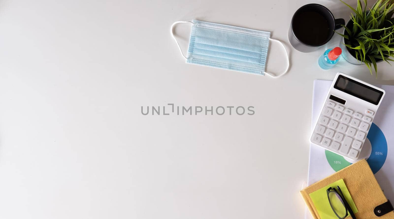 White office desk table with surgical face mask and sanitizer bottle or alcohol gel with calculator isolated on white background, work from home