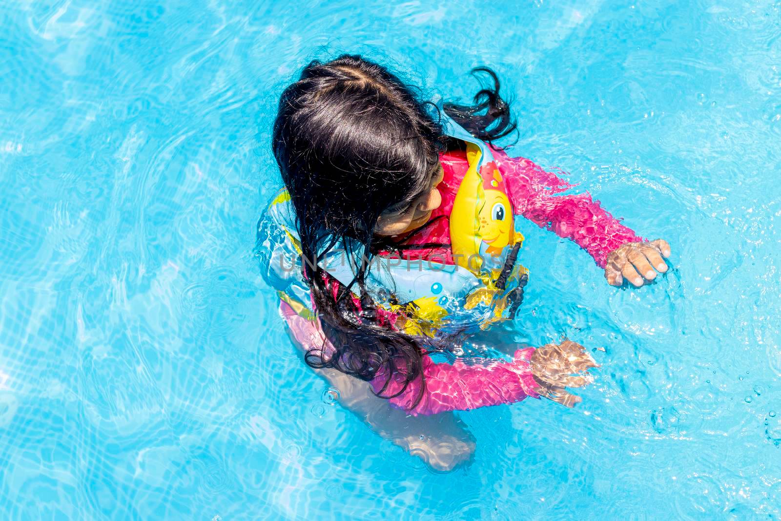 Little girl swimming with floaties, in the blue waters of a pool in the summer by eagg13