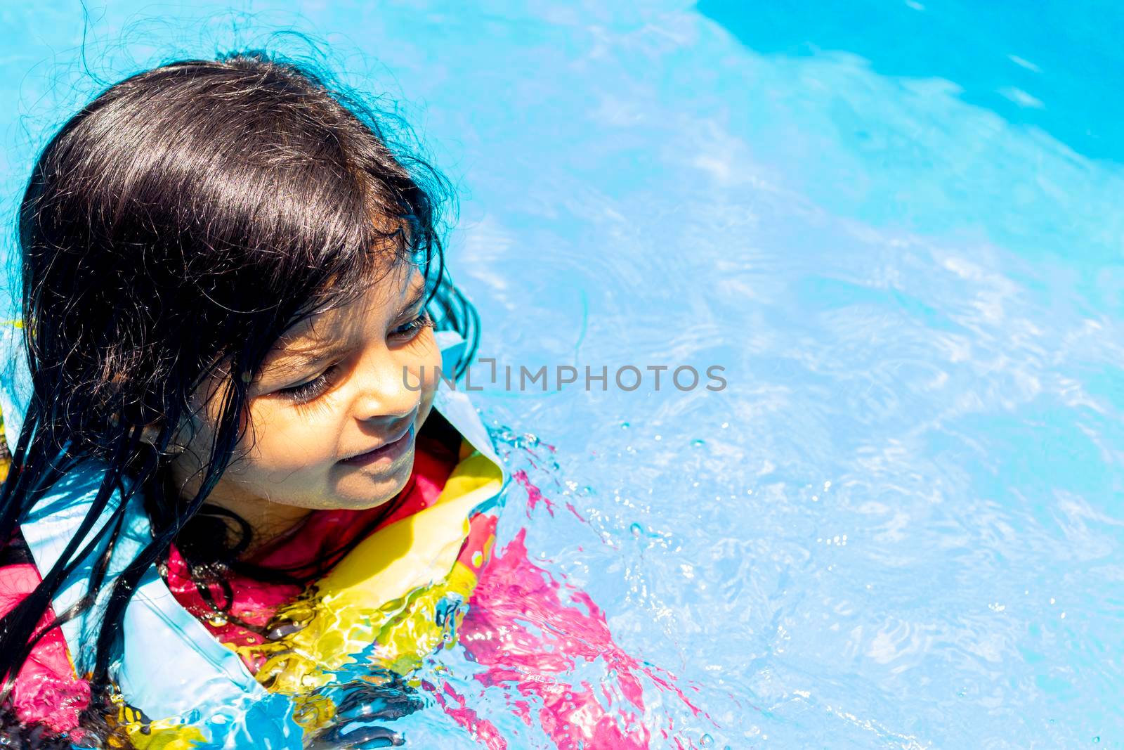 Little girl swimming with floaties, in the blue waters of a pool in the summer by eagg13