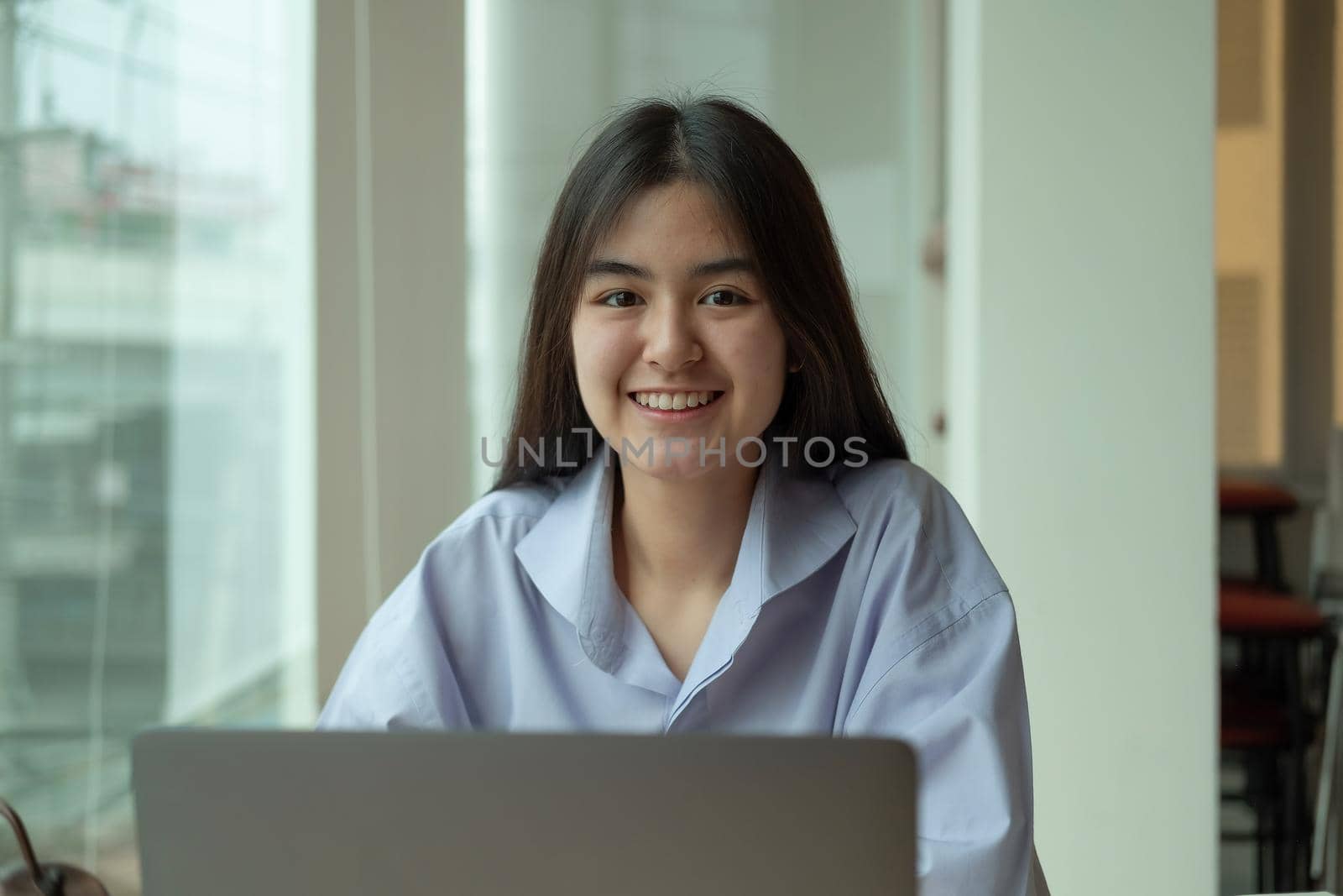 Portrait young asian girl looking camera while using laptop computer by nateemee