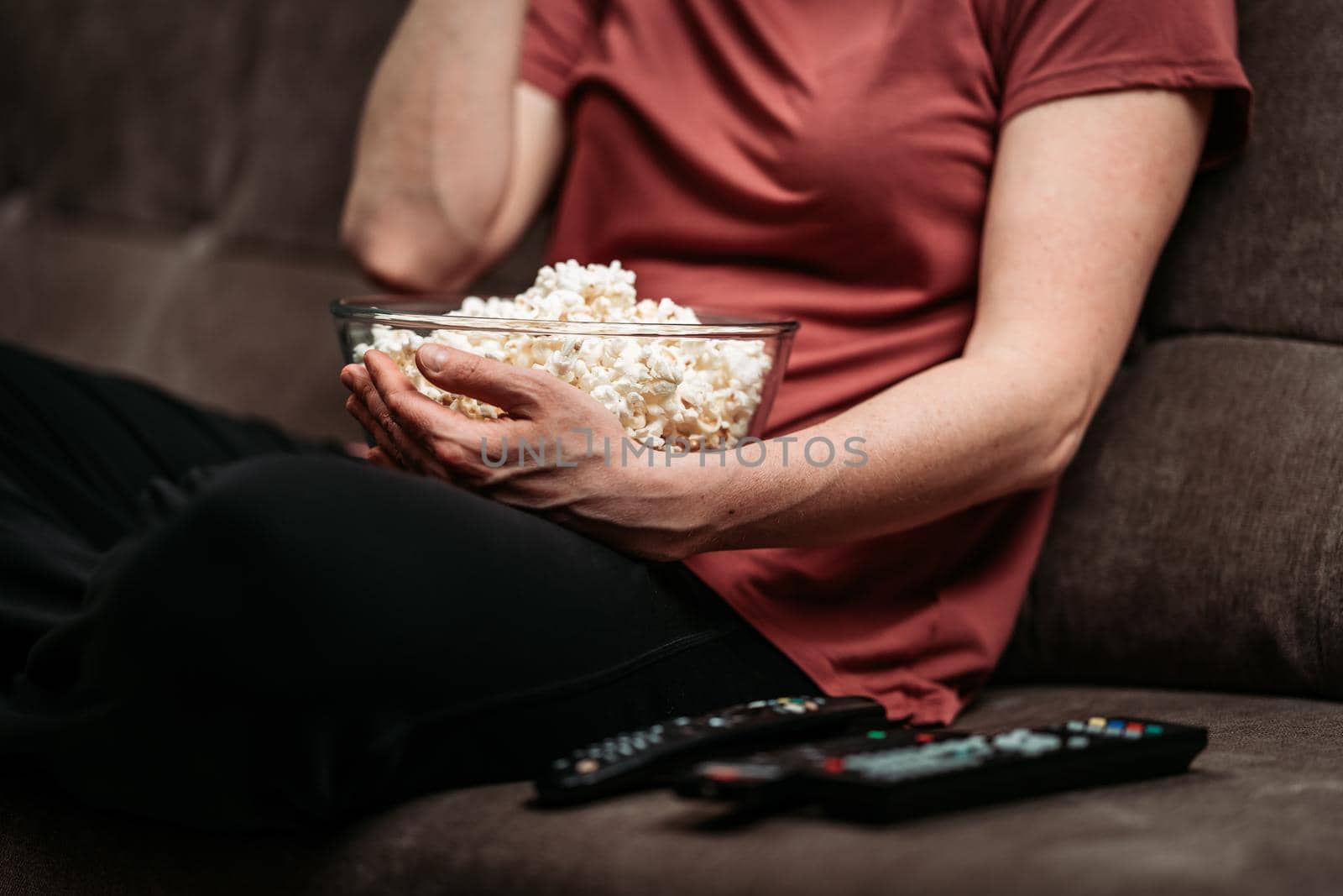 bowl with popcorn while watching a movie on TV. remote control on the sofa by Edophoto