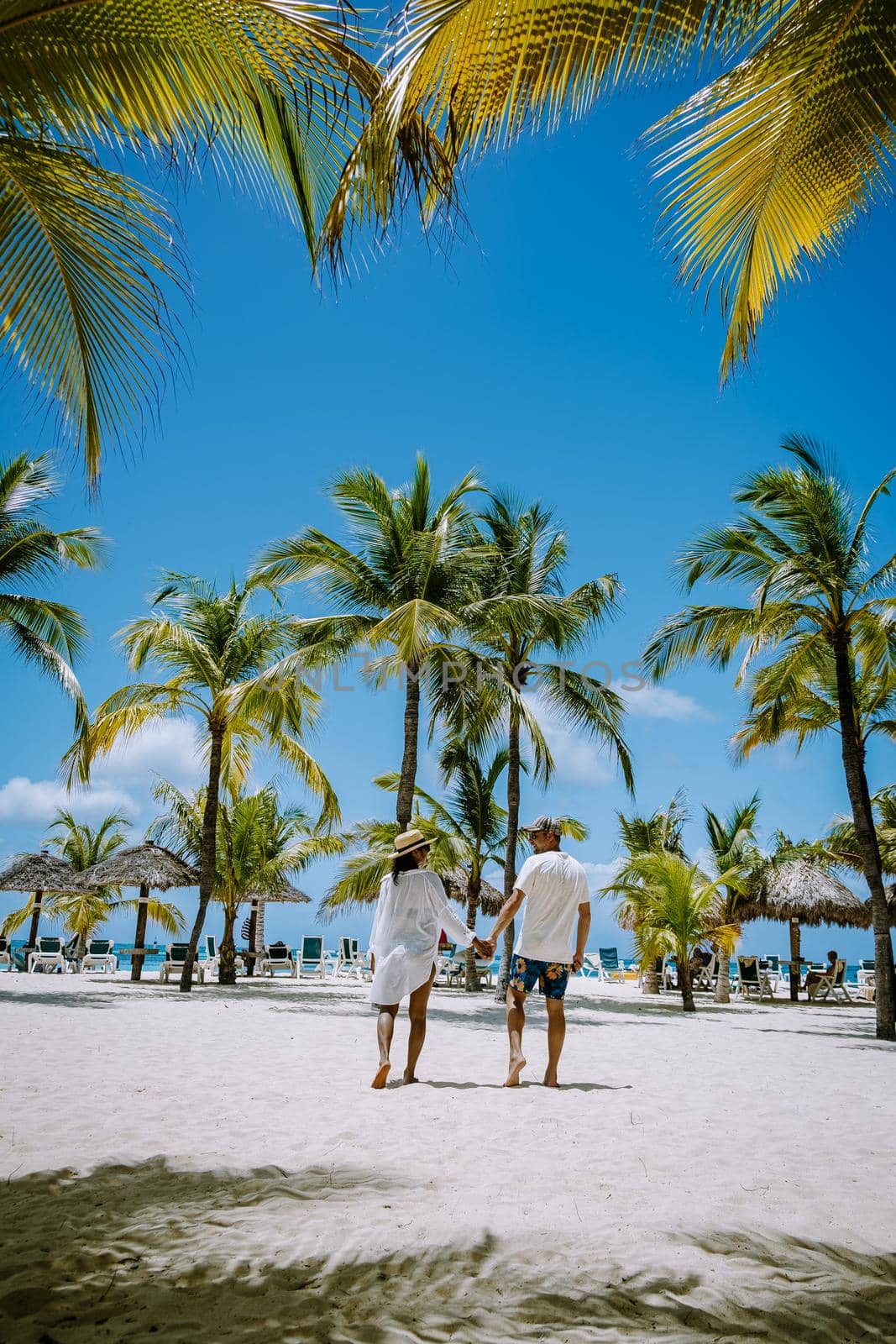 Palm Beach Aruba Caribbean, white long sandy beach with palm trees at Aruba Antilles, couple man and woman mid age on a white beach with palm trees