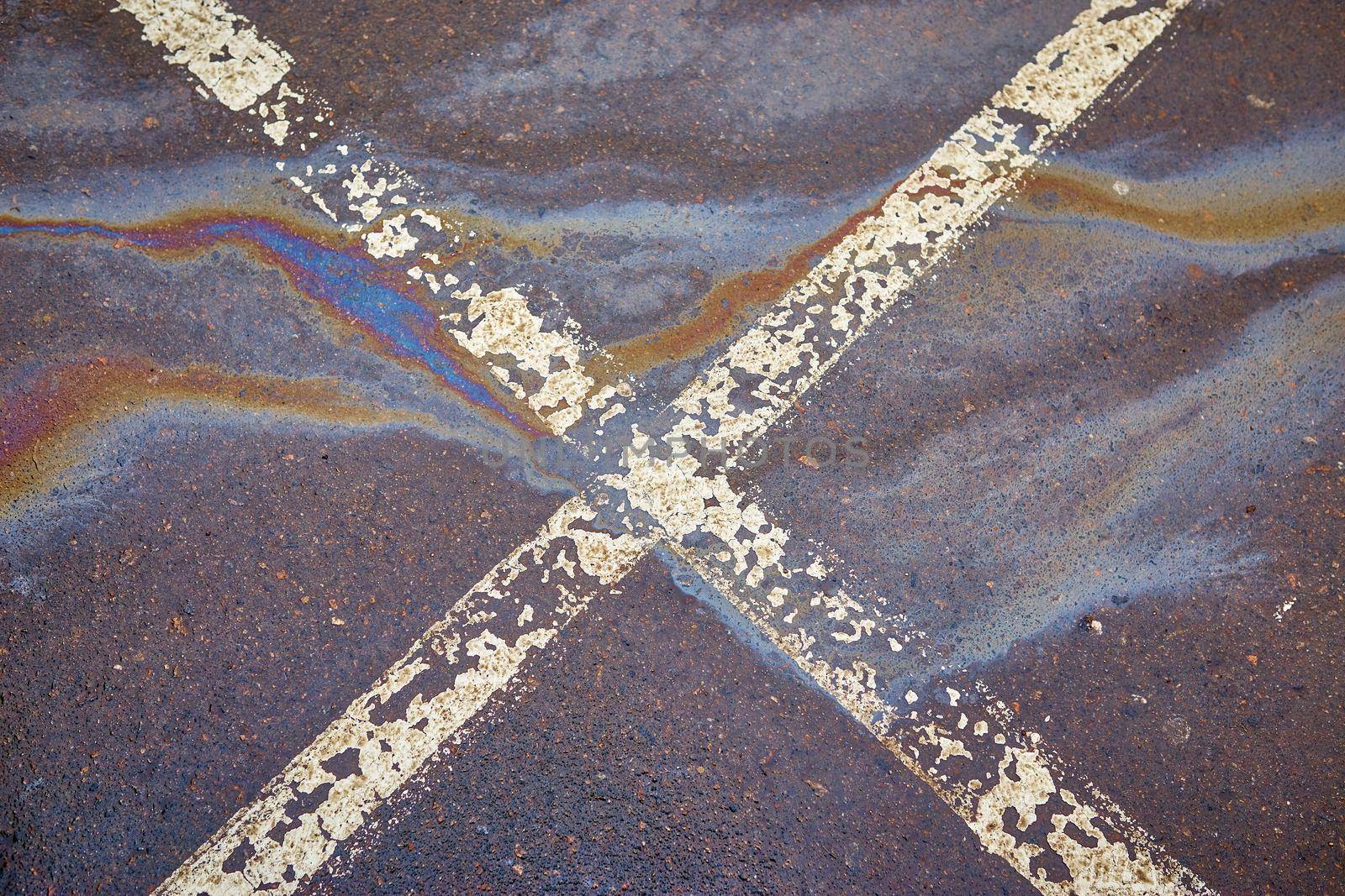 Gas stain on wet asphalt in the car park caused by a leak under a car or truck, abstract background