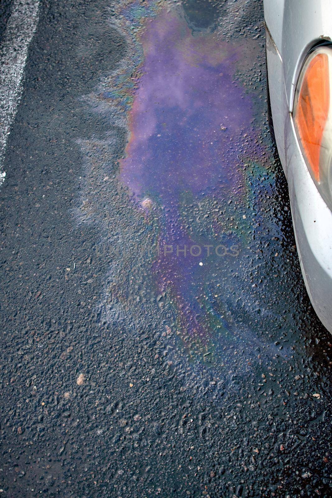 Colorful gas stain on wet asphalt. Oil stain caused by a leak under a car. Environmental pollution concept.