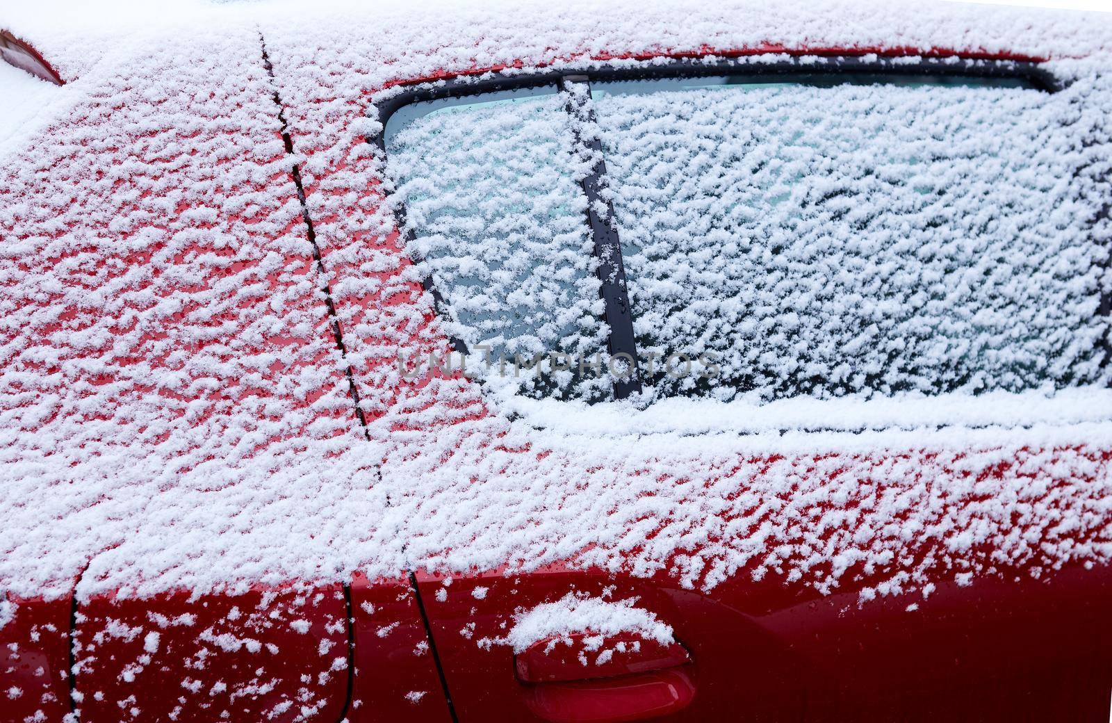 Snow-covered red car window, natural background, first snow. Close-up