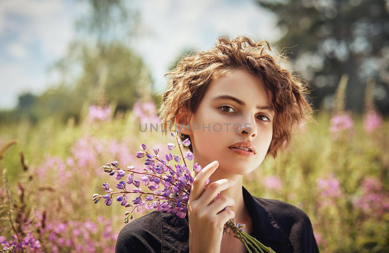 Young woman with a bouquet of lupines in her hand against the background of blooming Ivan-tea by AliaksandrFilimonau