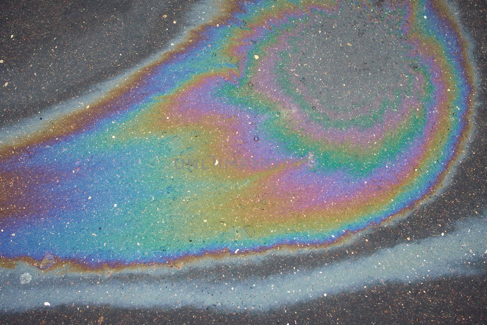 Abstract rainbow effect, colorful gas stain on wet asphalt.Rainbow gasoline leak after a car on a pedestrian sidewalk.