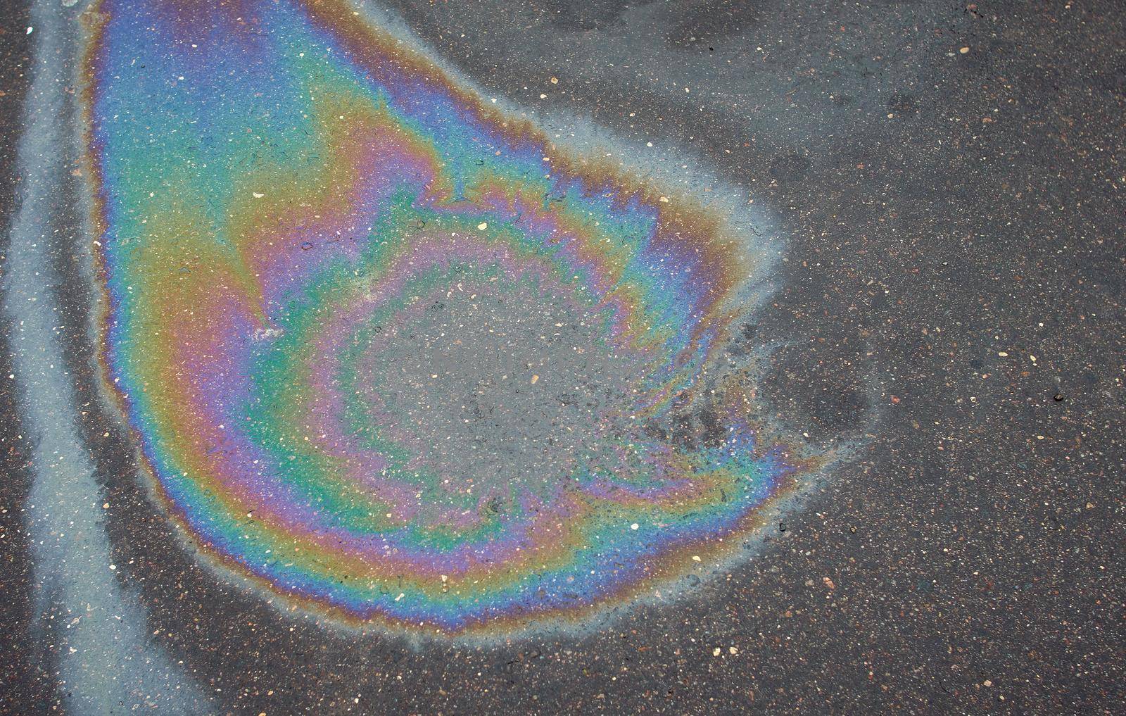 Abstract rainbow effect, colorful gas stain on wet asphalt.Rainbow gasoline leak after a car on a pedestrian sidewalk.