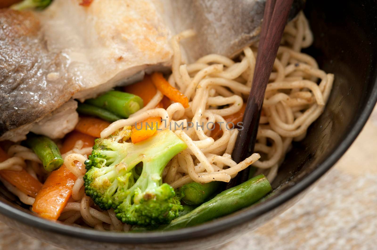 Healthy Asian fish and vegetable noodles in a close up view with broccoli and carrots served in a black bowl