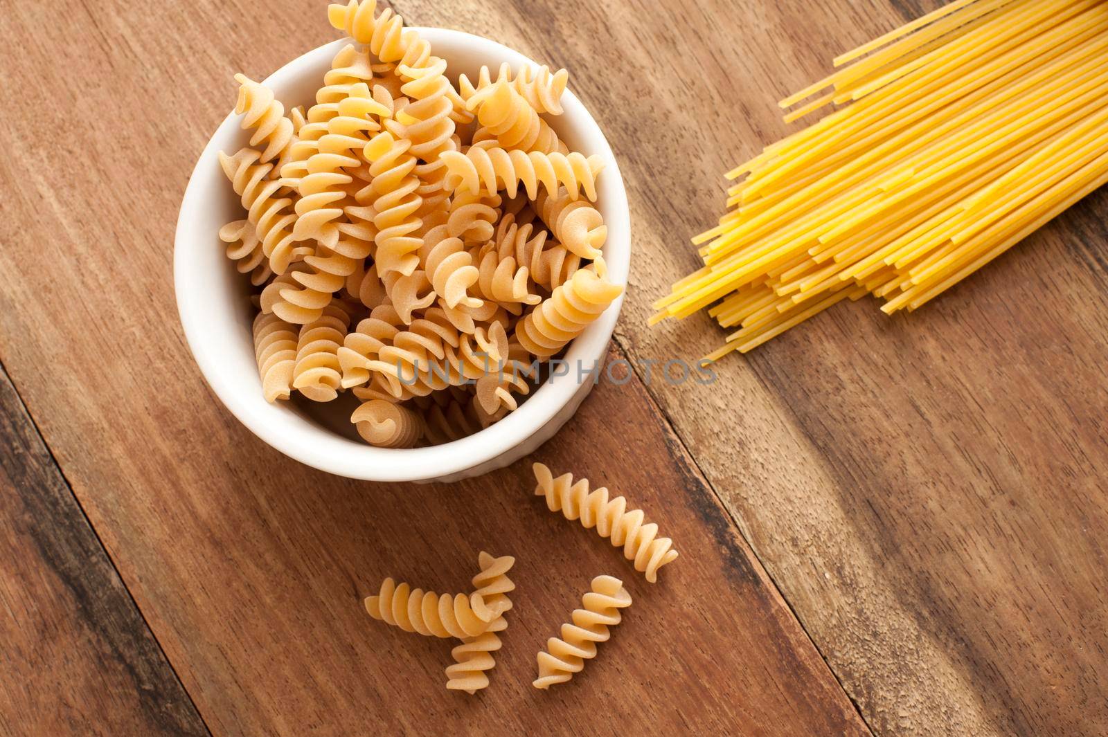 Dried Italian spiral fusilli and spaghetti pasta on a wooden kitchen table ready to be used as cooking ingredients in a Mediterranean recipe