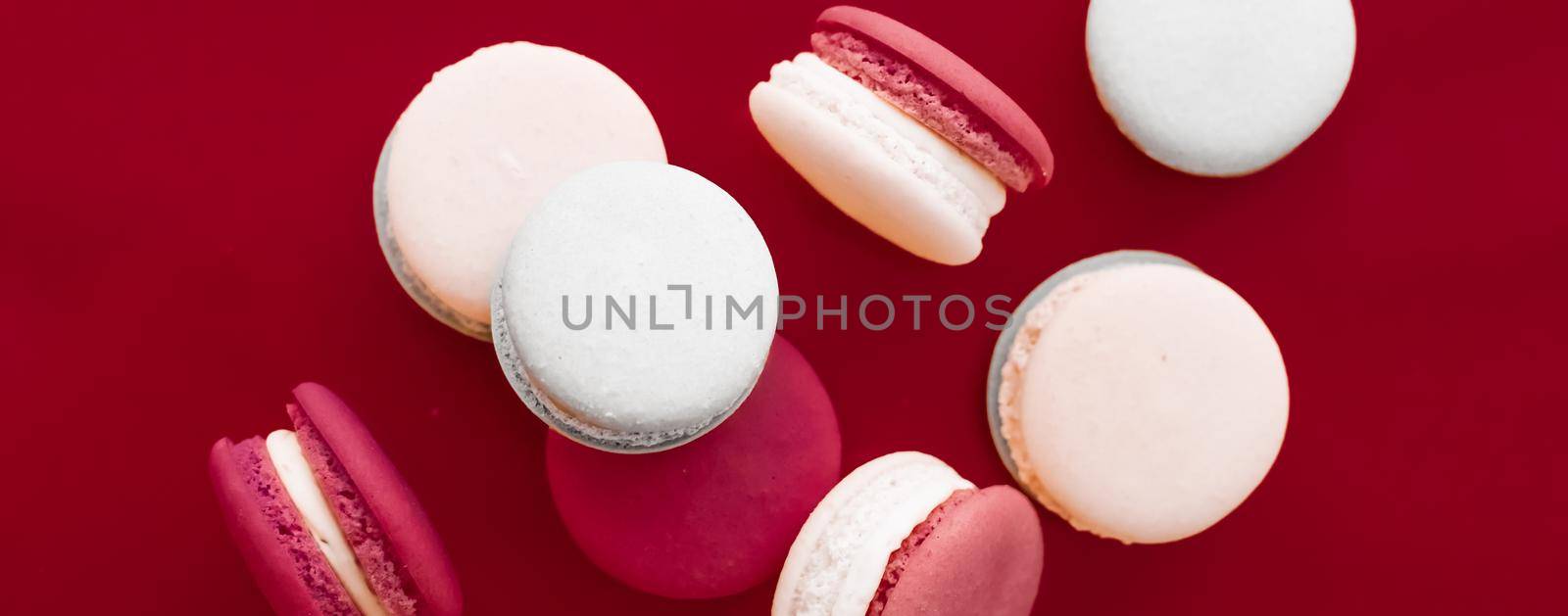 French macaroons on wine red background, parisian chic cafe dessert, sweet food and cake macaron for luxury confectionery brand, holiday backdrop design by Anneleven